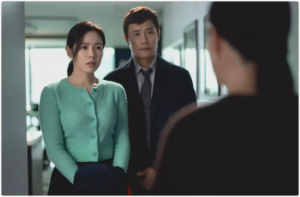 电影剧照显示办公室走廊场景,一名绿色开衫女性和西装男性面对另一人,体现职场紧张氛围