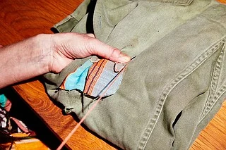 一只手正在为破旧的布料缝补彩色补丁,象征“patchy”原义——东补一块、西补一块、不完整的状态。