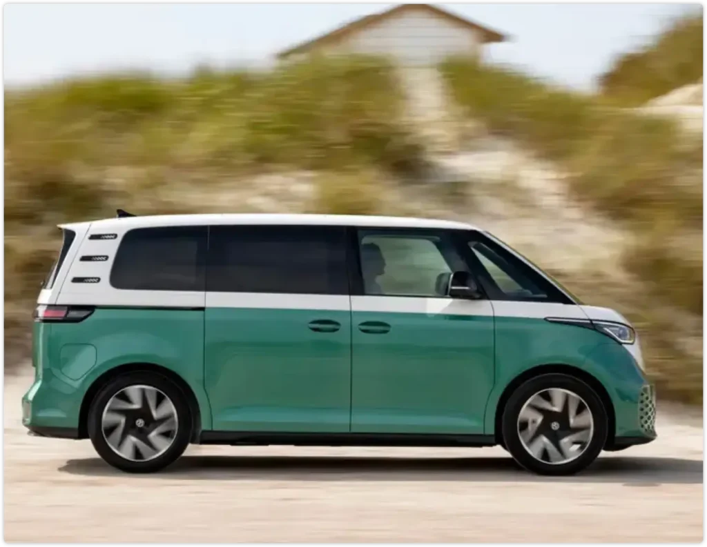 图片中是一辆正在沙丘旁的道路上疾驰的薄荷绿与白色相间的电动小巴（类似大众 ID. Buzz）。画面带有明显的运动模糊感，展现了现代生活方式和清洁能源出行的理念。